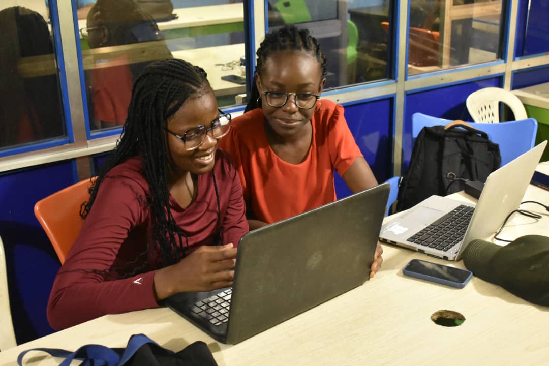 Two young women smiling as they work on a laptop