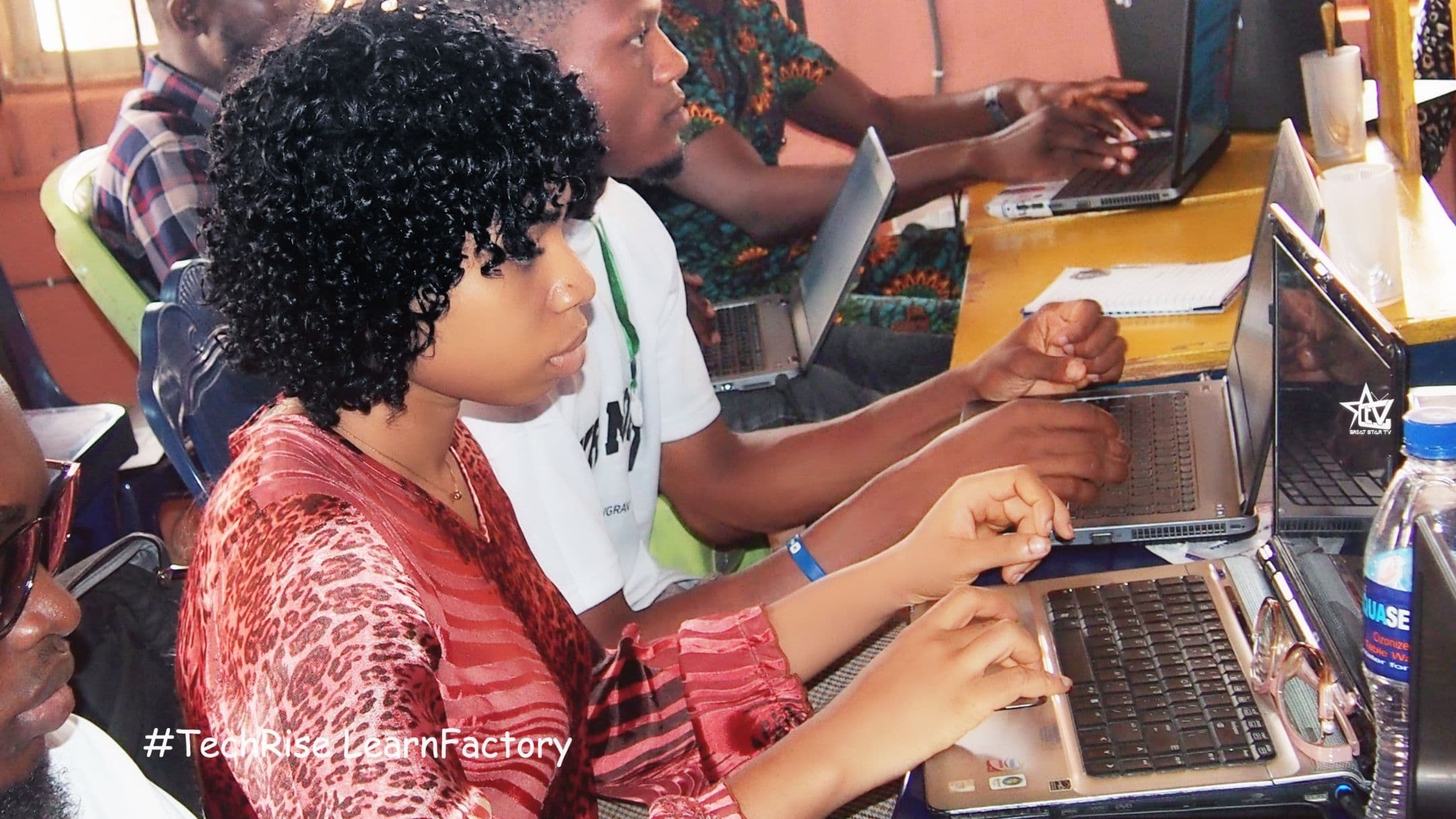 A learner coding on a laptop beside classmates